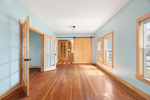 empty room with a barn door, wood-type flooring, and french doors