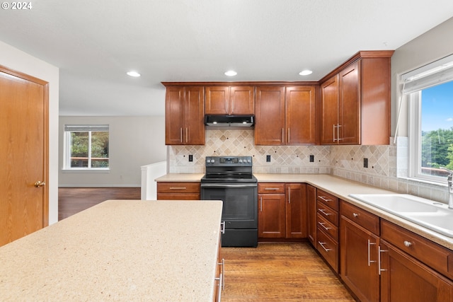 kitchen featuring light stone countertops, sink, light wood-type flooring, backsplash, and black / electric stove