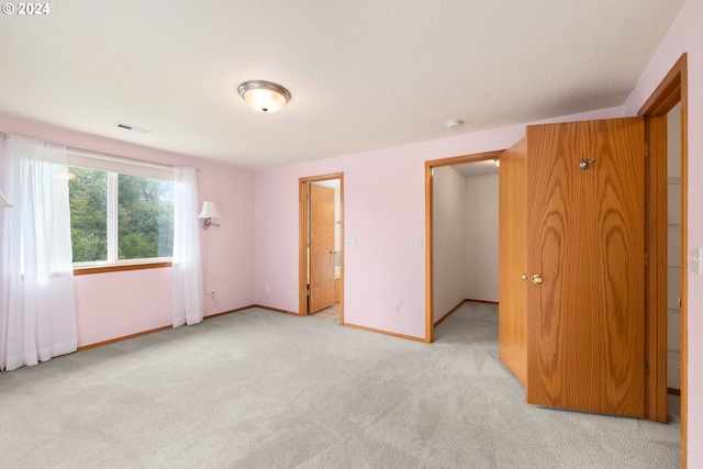 unfurnished bedroom with light carpet, a closet, and ensuite bath