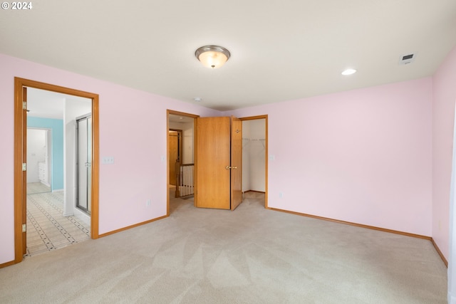 unfurnished bedroom with a closet, a spacious closet, and light colored carpet