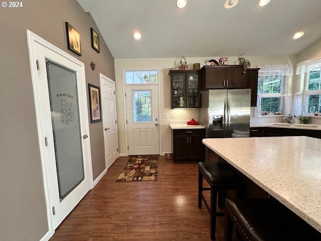 kitchen with dark hardwood / wood-style flooring, vaulted ceiling, dark brown cabinetry, sink, and stainless steel fridge