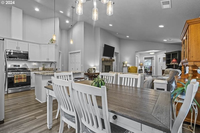 dining room with recessed lighting, wood finished floors, visible vents, a fireplace, and high vaulted ceiling