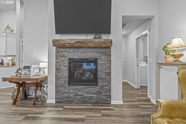 living room featuring wood finished floors, visible vents, baseboards, and a stone fireplace