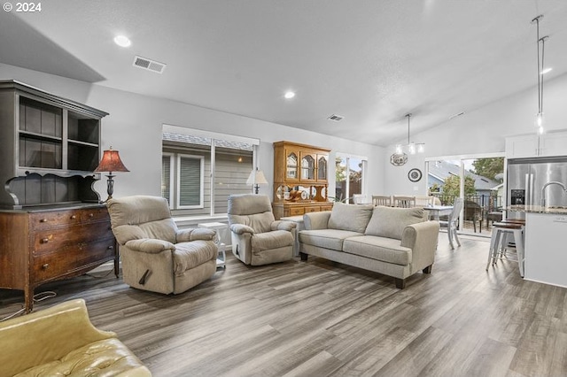 living room with vaulted ceiling, an inviting chandelier, and hardwood / wood-style floors