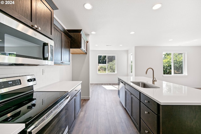 kitchen with sink, stainless steel appliances, an island with sink, light hardwood / wood-style floors, and dark brown cabinetry