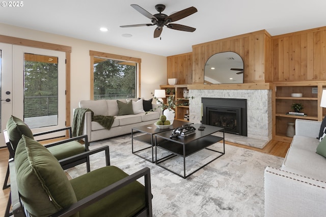 living room featuring light hardwood / wood-style floors, a stone fireplace, ceiling fan, and wood walls