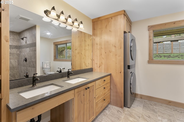 bathroom featuring vanity, toilet, stacked washer and dryer, and a tile shower