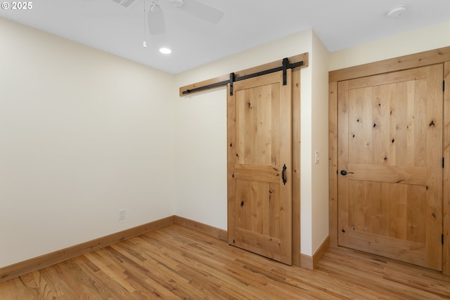 unfurnished bedroom with a barn door, ceiling fan, and light wood-type flooring