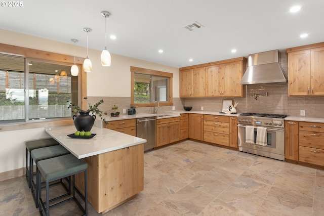 kitchen featuring a kitchen breakfast bar, wall chimney range hood, hanging light fixtures, appliances with stainless steel finishes, and kitchen peninsula