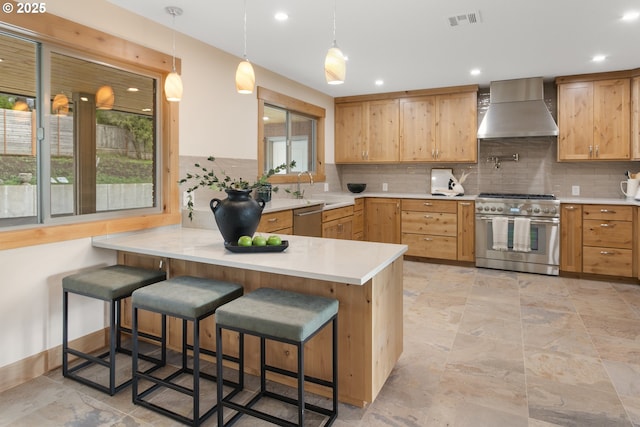 kitchen with kitchen peninsula, appliances with stainless steel finishes, a kitchen breakfast bar, and wall chimney range hood