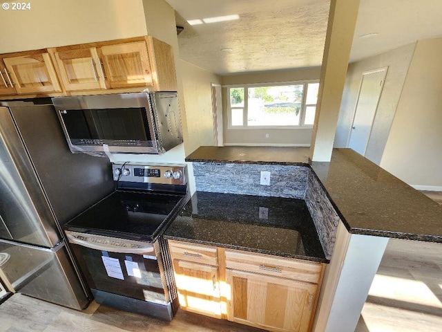 kitchen featuring kitchen peninsula, dark stone counters, and appliances with stainless steel finishes