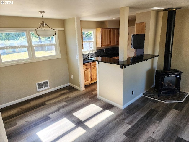 kitchen featuring kitchen peninsula, pendant lighting, dark hardwood / wood-style flooring, a wood stove, and backsplash