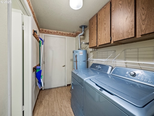 washroom featuring light wood-type flooring, strapped water heater, cabinets, washing machine and dryer, and a textured ceiling