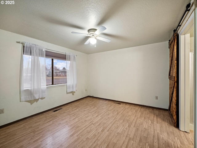 unfurnished bedroom with ceiling fan, a barn door, a textured ceiling, and light wood-type flooring