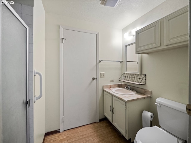 bathroom featuring wood-type flooring, vanity, toilet, a shower with door, and a textured ceiling