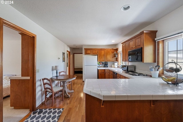 kitchen with tile countertops, kitchen peninsula, white appliances, and light hardwood / wood-style flooring