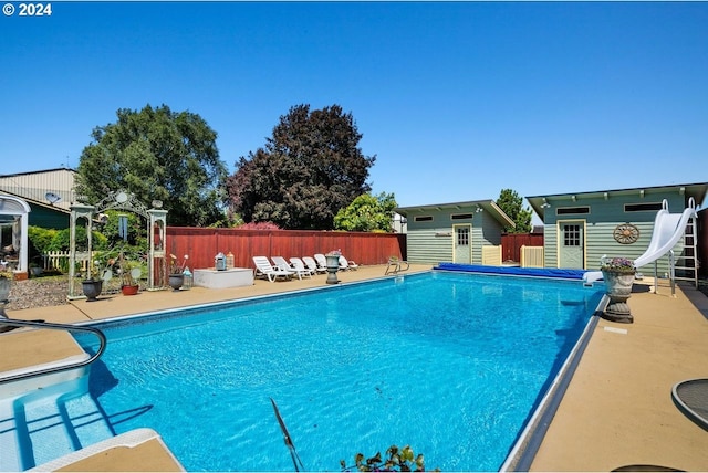 view of pool featuring a patio area, a water slide, and a storage unit