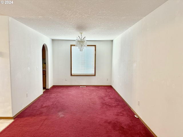 carpeted empty room with a chandelier and a textured ceiling