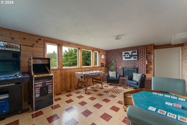 game room featuring wooden walls, light floors, and a brick fireplace