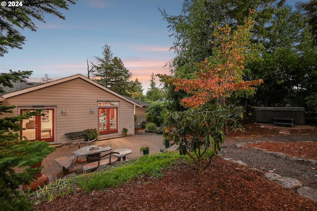 back of house at dusk with a patio, french doors, an outdoor fire pit, and a hot tub