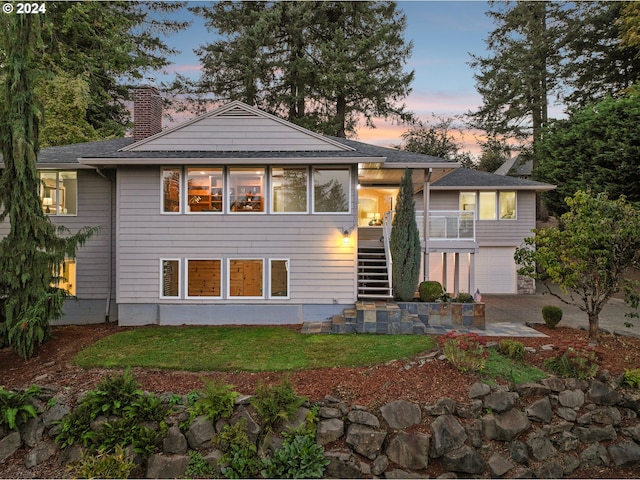 view of front of property with stairway, an attached garage, a chimney, a patio area, and a lawn