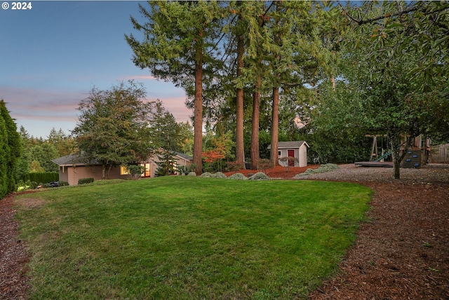 yard at dusk with an outbuilding, a storage shed, and a playground