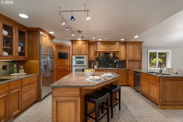 kitchen featuring a sink, dark stone countertops, a kitchen island, appliances with stainless steel finishes, and brown cabinetry