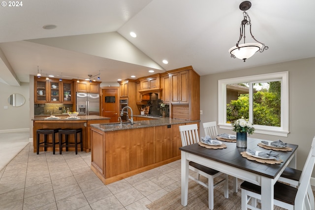 kitchen featuring a peninsula, brown cabinetry, lofted ceiling, and stainless steel appliances