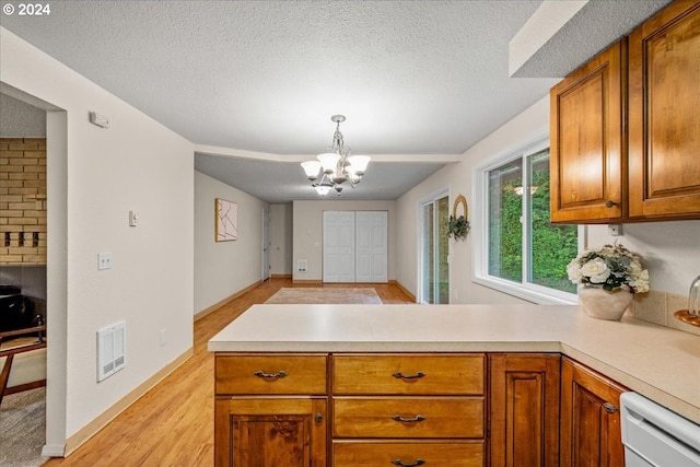 kitchen with kitchen peninsula, a textured ceiling, decorative light fixtures, dishwasher, and light hardwood / wood-style floors