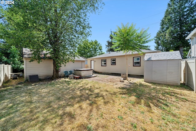 back of house with a lawn, a hot tub, and a storage unit