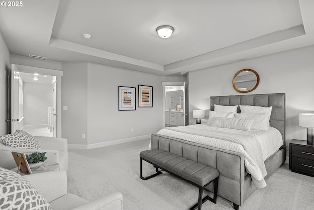 bedroom with a raised ceiling, light carpet, and ensuite bath