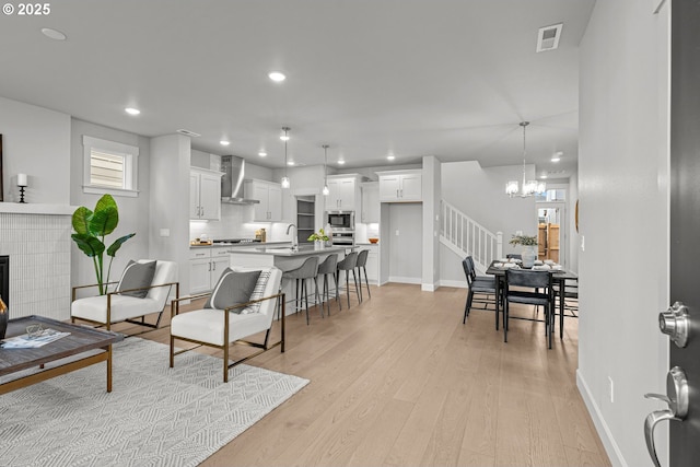 living room featuring a chandelier, sink, a tiled fireplace, and light hardwood / wood-style floors