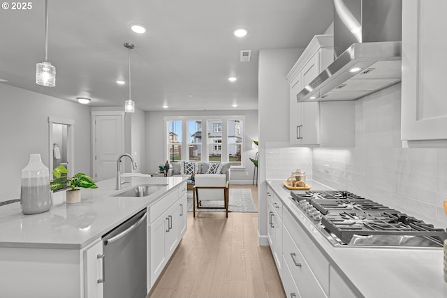 kitchen with pendant lighting, white cabinetry, sink, stainless steel appliances, and wall chimney range hood