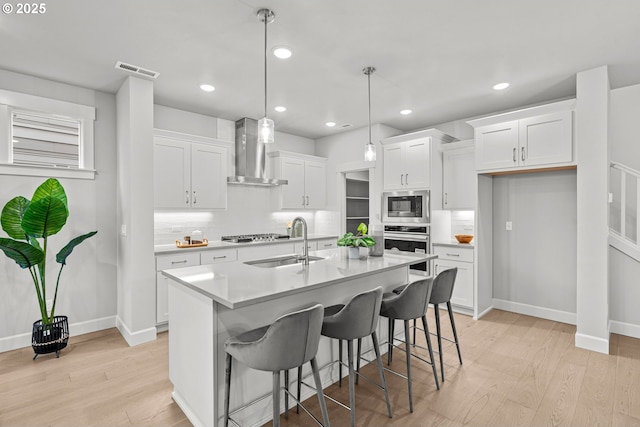 kitchen featuring sink, hanging light fixtures, appliances with stainless steel finishes, wall chimney range hood, and white cabinets