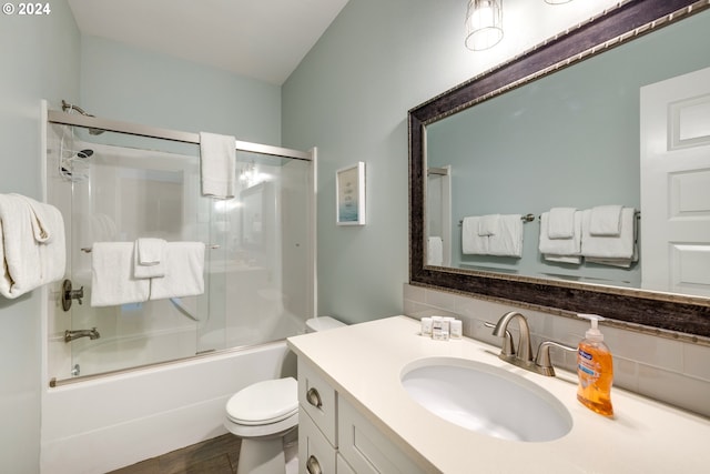 full bathroom with bath / shower combo with glass door, vanity, toilet, and tasteful backsplash