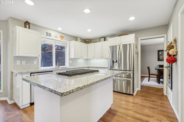 kitchen with sink, light hardwood / wood-style flooring, decorative backsplash, appliances with stainless steel finishes, and a kitchen island