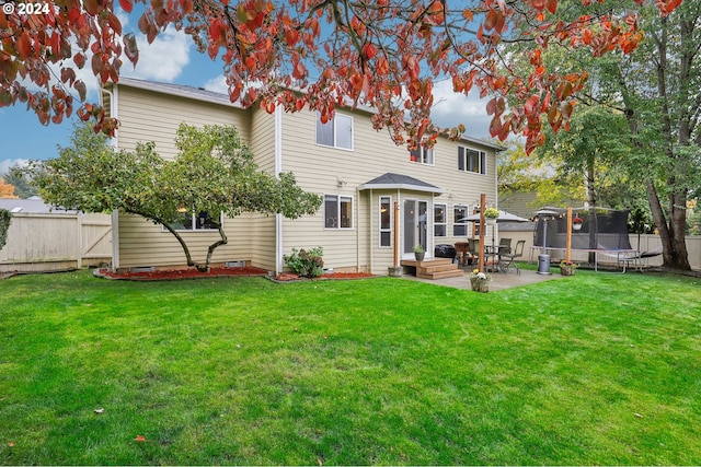 rear view of property featuring a yard, a patio, and a trampoline