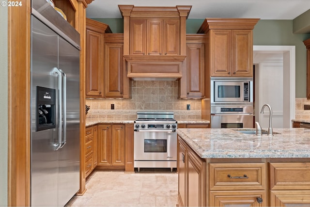 kitchen featuring decorative backsplash, built in appliances, light stone counters, and sink