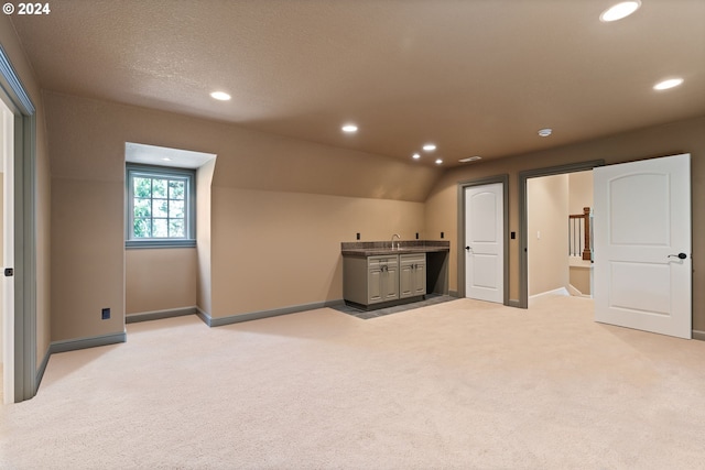 interior space featuring a textured ceiling, sink, light carpet, and vaulted ceiling