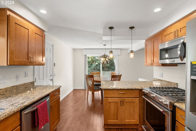 kitchen featuring light stone counters, kitchen peninsula, dark wood-type flooring, decorative light fixtures, and stainless steel appliances