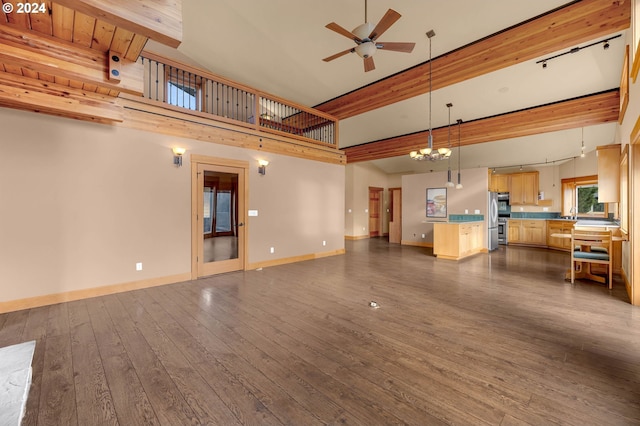 unfurnished living room featuring ceiling fan with notable chandelier, a high ceiling, dark hardwood / wood-style flooring, and beam ceiling