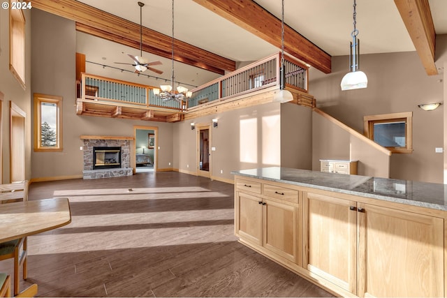 kitchen featuring dark wood-type flooring, a high ceiling, hanging light fixtures, a fireplace, and light brown cabinetry