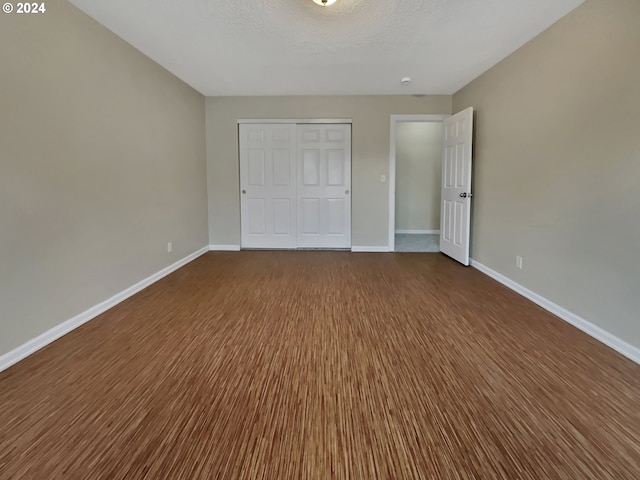 unfurnished bedroom with a textured ceiling, dark wood-type flooring, and a closet