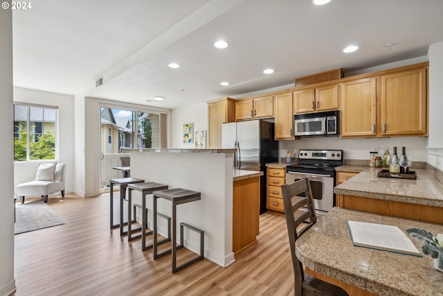 kitchen featuring a breakfast bar area, light brown cabinets, light wood-type flooring, a kitchen island, and appliances with stainless steel finishes