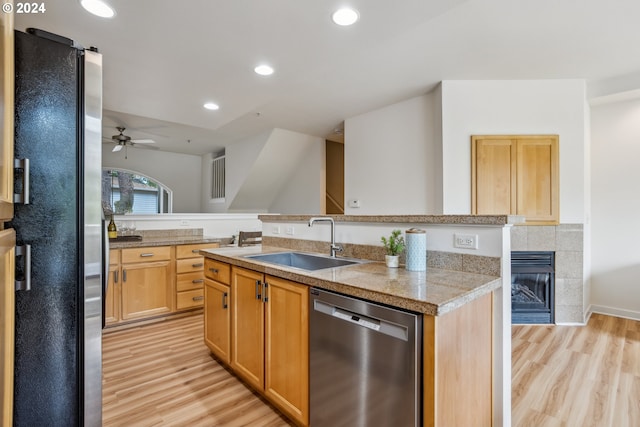 kitchen with appliances with stainless steel finishes, sink, light hardwood / wood-style floors, a tiled fireplace, and ceiling fan