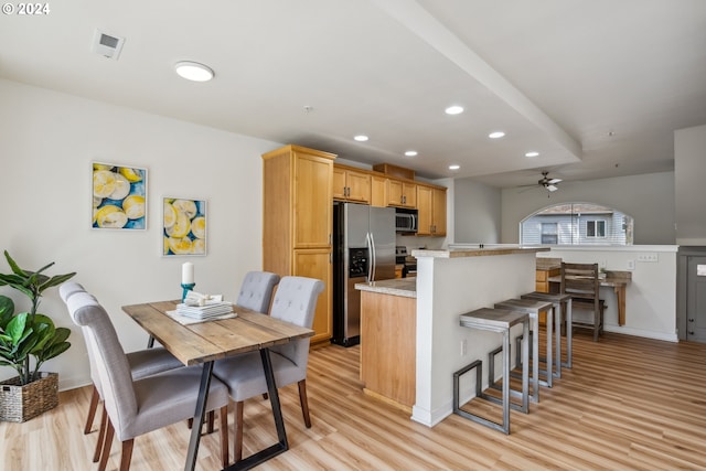 kitchen featuring light brown cabinetry, ceiling fan, light hardwood / wood-style floors, appliances with stainless steel finishes, and a kitchen breakfast bar