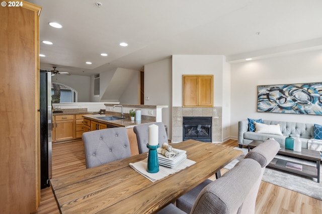 dining space featuring a tile fireplace, sink, light wood-type flooring, and ceiling fan