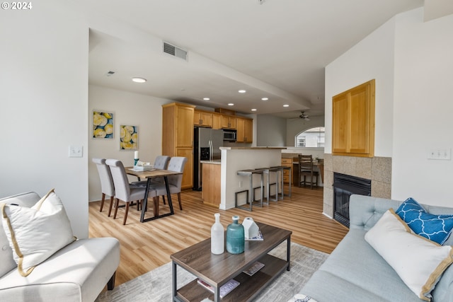 living room with light hardwood / wood-style floors, a tiled fireplace, and ceiling fan