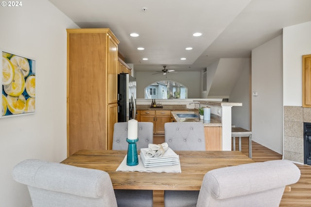 dining area with sink, a tiled fireplace, ceiling fan, and light wood-type flooring