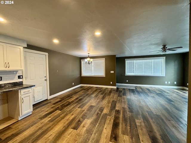 unfurnished living room featuring ceiling fan with notable chandelier and dark wood-type flooring